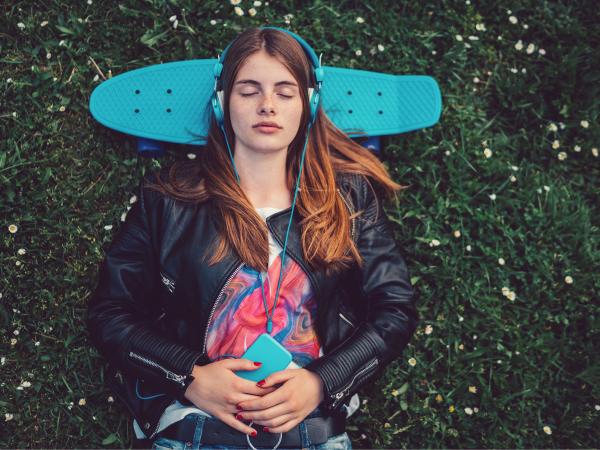 Young person laying on grass with a skateboard under their head