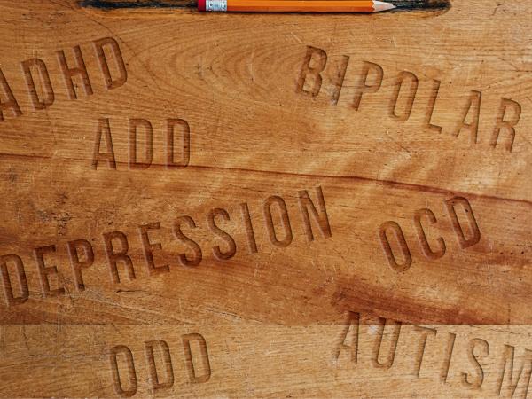 Wooden desktop with words engraved ADHD, Bipolar, ADD, Depression, OCD, ODD and Autism