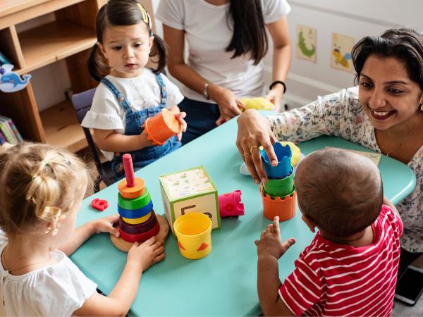 woman smiling and playing with blocks with 3 children